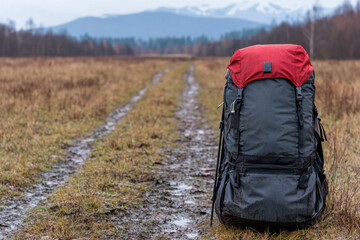 A large black backpack sits on a muddy road in the middle of a field