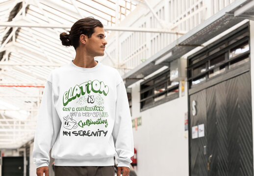 A man wearing a  jumper stands in a spacious indoor area while preparing for a logo mockup, showcasing design potential.