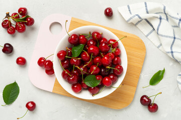 Fresh cherries in bowl on concrete background, top view