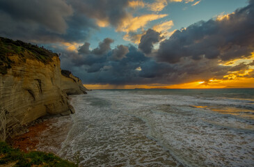 Dramatic sunset over coastal cliffs and turbulent sea.