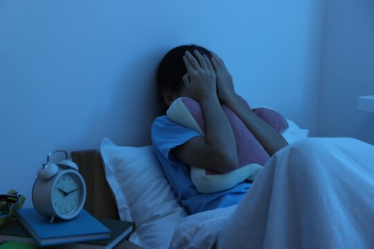 Afraid girl covering face with hands in bed at night