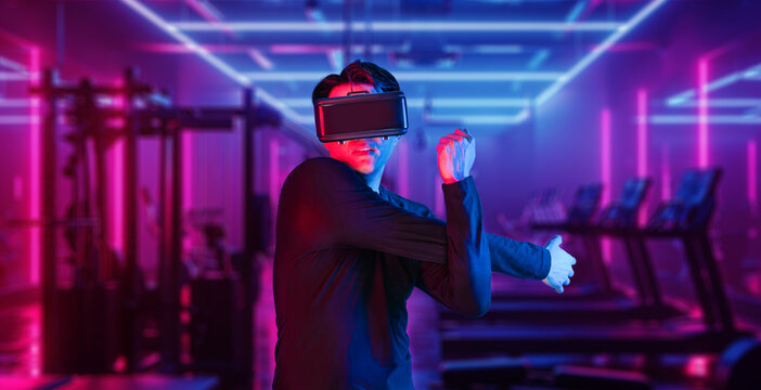 Asian man with VR glasses playing fitness while exercising at fitness. Male model using augmented reality and artificial intelligence to plan exercise plan. Technology innovation concept. Ingenuity.