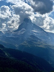 Majestic Matterhorn in summer, surrounded by green grass, hiking trails, and drifting clouds — a...