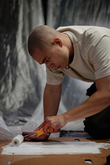 Side view of male artist with buzz cut fully immersed in creation of designer clothes painting with...