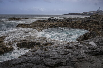 Dramatic coastal scene in Gran Canaria with waves crashing against dark volcanic rocks. El Bufadero