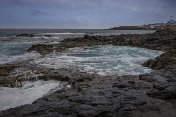 Dramatic coastal scene in Gran Canaria with waves crashing against dark volcanic rocks. El Bufadero