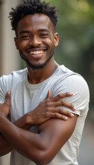 A cheerful young Black man with a bright smile stands confidently, arms crossed, exuding warmth and positivity. His relaxed demeanor and engaging expression create an inviting atmosphere, perfect for
