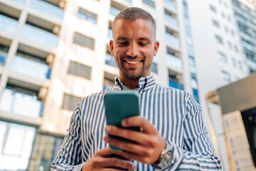 Young entrepreneur smiling and checking his phone in front of buildings