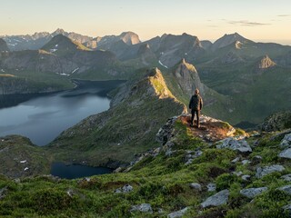 A hiker on the peak of a grassy mountain at sunset. 