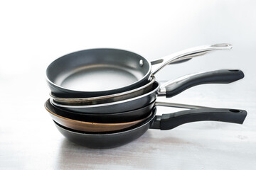 Stack of various frying pans made from cast iron, carbon steel, non-stick coated and stainless steel, choosing the right kitchen ware, light gray background, copy space