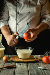 A skilled chef prepares a delicious dessert, carefully slicing a vibrant apple while surrounded by creamy ingredients in a charming and rustic kitchen setting, illuminated by warm light