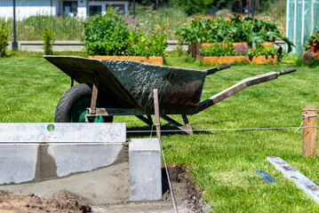 A wheelbarrow filled with liquid concrete mixed by hand in a freestanding concrete mixer.