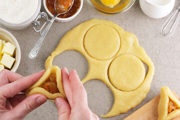 Hands skillfully shape triangular a sweet pastry in a warm kitchen fruit filling other baking ingredients. Traditional Jewish Hamantaschen pastries with apricot jam. top view