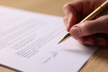 Woman putting signature on document at table, closeup