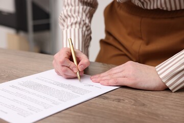 Woman putting signature on document at wooden table, closeup