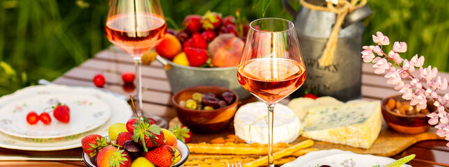 Banner. Countryside beautiful wedding decor, surprise romantic date outdoors, garden arrangement with lupins flowers on a meadow. Fruits, rose wine, burning candles. Sunset, candlelight, golden hour
