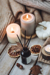 Hello autumn, cozy slow living. Pumpkin, aromatic candle, warm sweaters, dry fall leaves, cinnamon, anise in golden lights with bokeh on white wooden background. Thanksgiving apartment decor