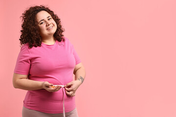 Happy plus size woman measuring waist with tape and holding pile of weight loss supplements on pink...