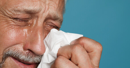 Sad senior man crying on light blue background, closeup