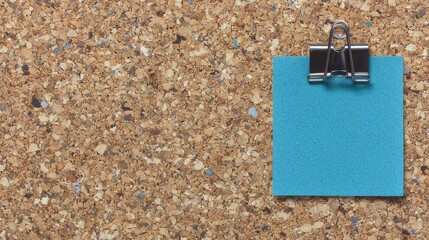 Color paper note pinned to brown cork board. Sticky post with large black clip on corkboard