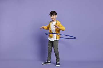 Boy exercising with hula hoop on violet background