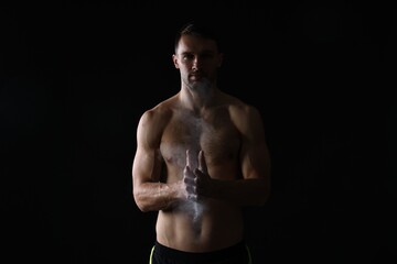 Fototapeta premium Man clapping hands with talcum powder before training on black background