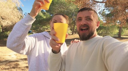 Happy couple celebrates friendship day with a cheerful toast using yellow cups in a park, capturing joyful moments of their bond amidst nature's embrace.International friendship day