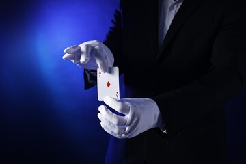 Illusionist with playing card on dark blue background, closeup
