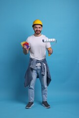 Man wearing hardhat with roller and color samples on blue background