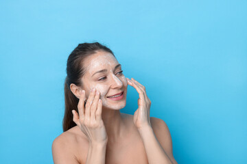 Spa day. Happy woman applying mask onto her face on light blue background