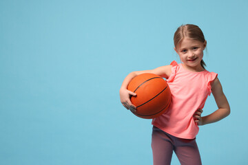Cute little girl with basketball ball on light blue background, space for text