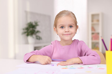 Cute girl at white table with drawing and pencils in kindergarten