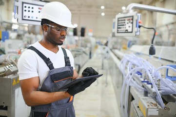 African male engineer. Control a material production machine system, working in a plastic and steel...