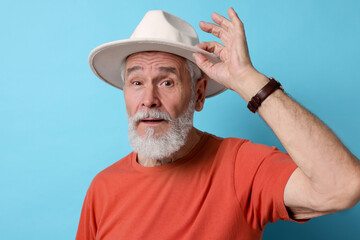 Stylish senior man in hat on light blue background
