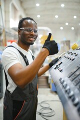 African male engineer. Control a material production machine system, working in a plastic and steel...