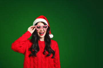 Beautiful woman in Santa hat and party glasses on green background, space for text. Christmas celebration