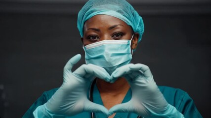 Surgeon in personal protective equipment, masked and showing a heart sign with both hands.