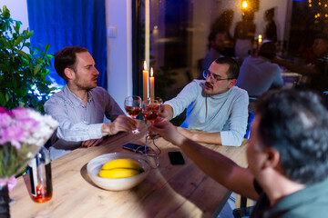 Friends enjoying a dinner gathering, sharing moments and toasting drinks at a cozy table with a warm atmosphere.