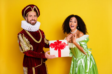 Joyful Couple in Period Costumes Sharing a Gift Against a Bright Yellow Background