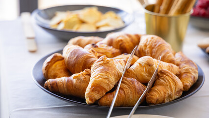 Many croissants on a plate at an event or banquet. Tongs for picking them up seen nearby.