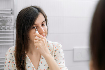 Beauty routine at home. Portrait of beautiful girl applying cream under eye with finger. Dark circles and anti-wrinkle concept.