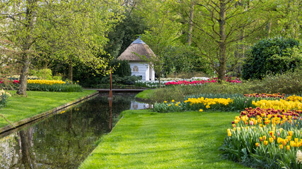 Scenic view of Keukenhof gardens in Lisse, Netherlands with bright flower display, canal and hut.