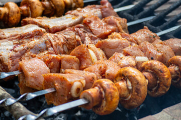 Grilled pieces of pork meat and mushrooms on metal skewers. Shashlik or shish kebab prepared on barbecue grill over hot charcoal with grilled vegetables.