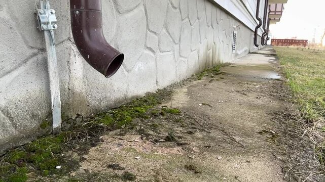 Brown stainless steel drain pipe for drain pipe with water drainage from roof the house to the ground. It attaches to a wall of residential building and leading to concrete surface