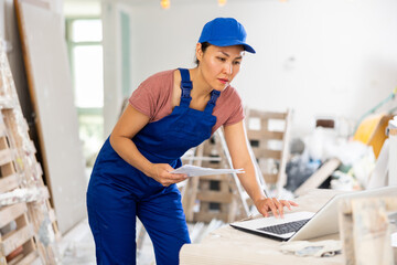 Female asian engineer matching check list, using laptop during repair works in house.