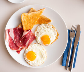 Delicious fried sunny side up eggs served with slices of ham and crisp roasted wheat bread toasts..
