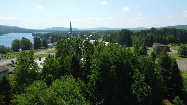 Drone flight at treetop level passing the steeple of the historic church in the lush village of Saint‑Z&eacute;non‑du‑Lac‑Humqui, Matapedia Valley, Quebec, Canada
