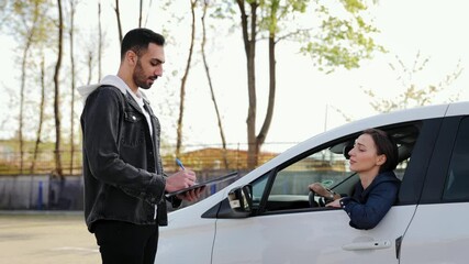 Driving instructor taking some notes about the passing of the driving test or the exam. Woman improves parking skills during practical courses at driving school