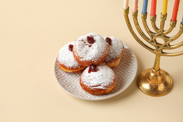 Menorah and plate with tasty donuts for Hanukkah celebration on beige background