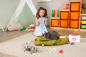 Naklejka premium Cute little girl with British cat, toy and first aid kit at home
